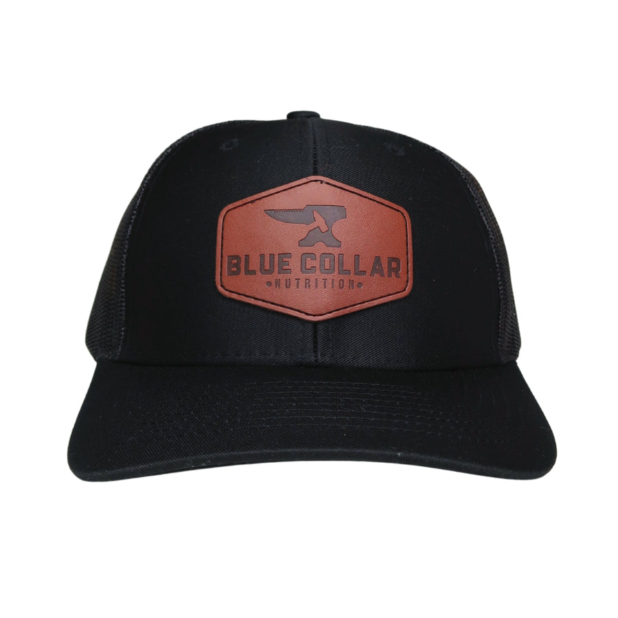 BCN Classic Trucker Curved Hat in solid black with hexagonal cognac leather patch sewn onto the front panel — front view
