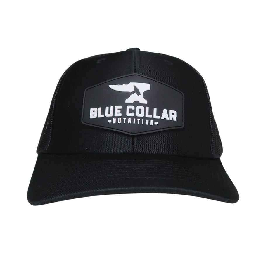 BCN Classic Trucker Curved Hat in black with hexagonal 3D PVC patch — raised white Blue Collar Nutrition logo on black rubberized background, front view