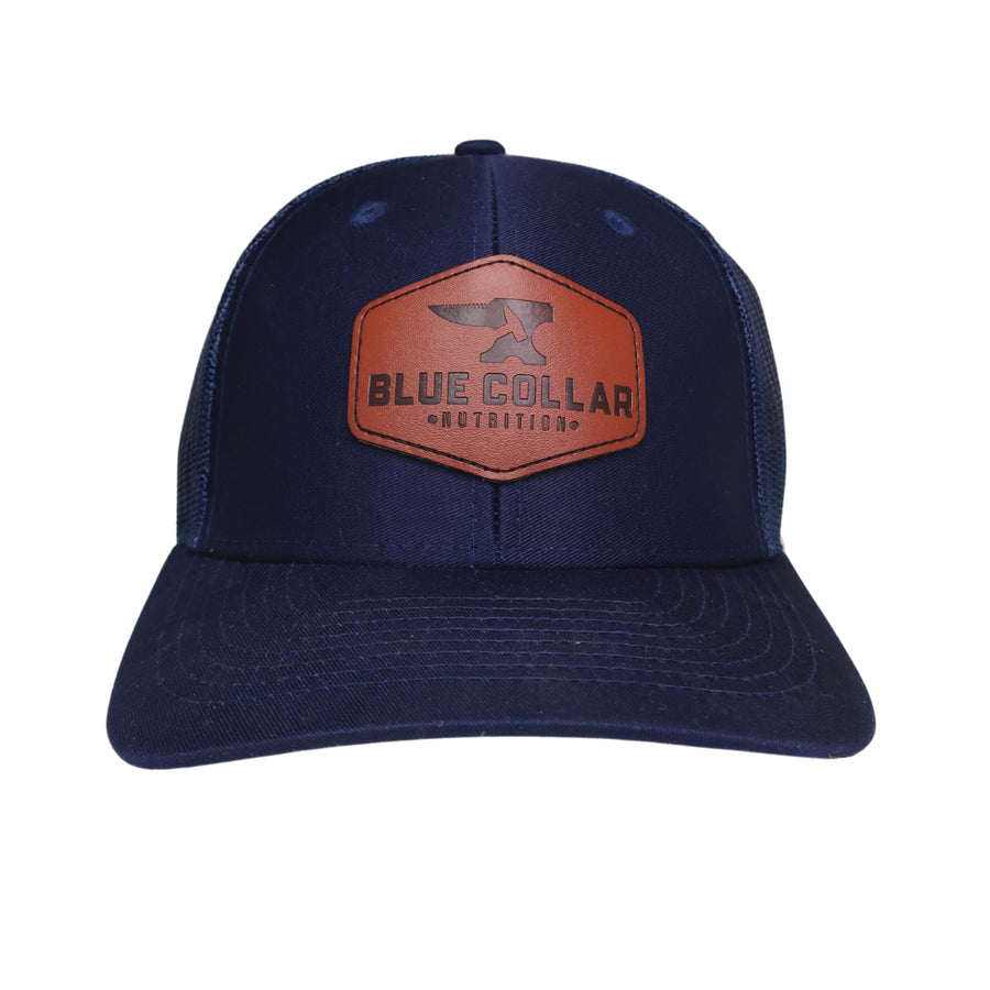 BCN Classic Trucker Curved Hat in solid navy blue with hexagonal cognac leather patch — front view of leather patch trucker hat